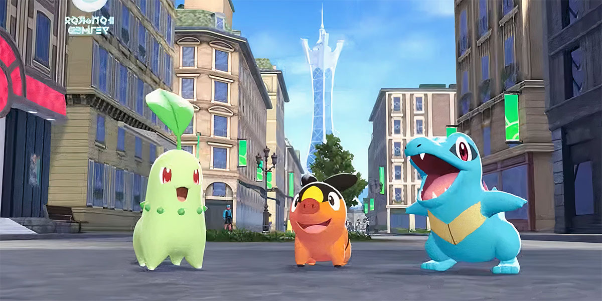 From left to right, the Pokémon Chikorita, Tepig and Totodile face the camera on a city street. A tall blue building, Lumiose Tower, is in the background.